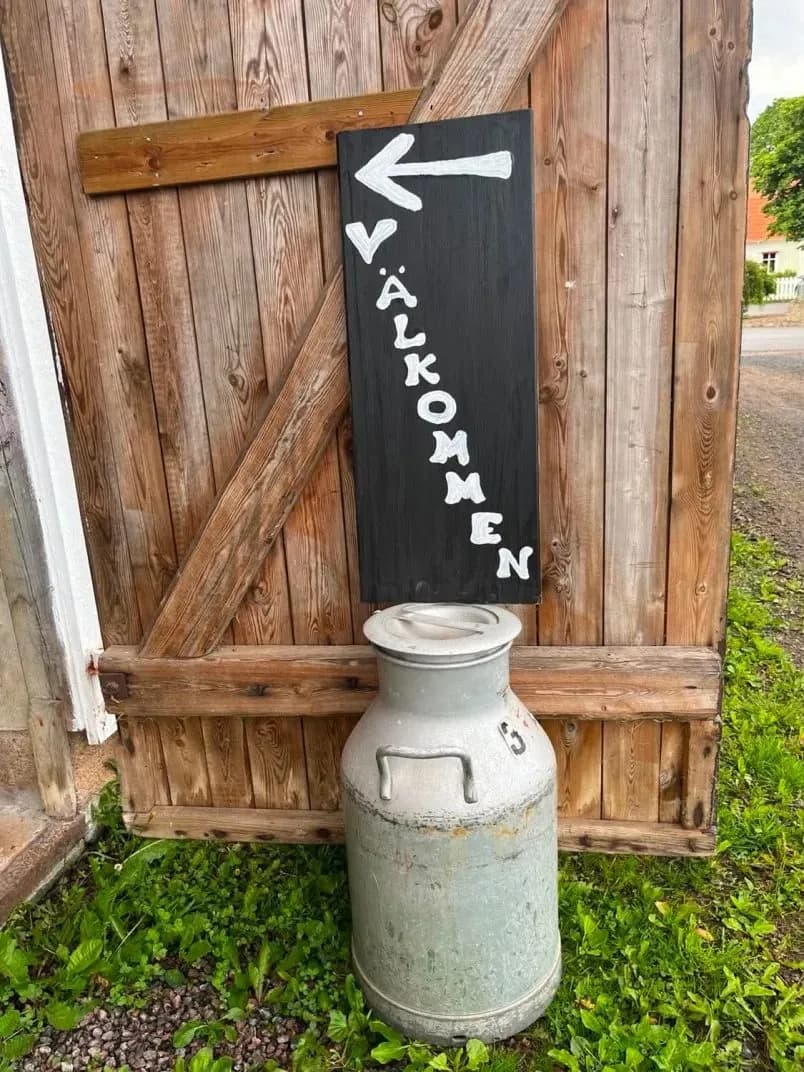 Handmålad VÄLKOMMEN-skylt med pil på en gammal mjölkkanna